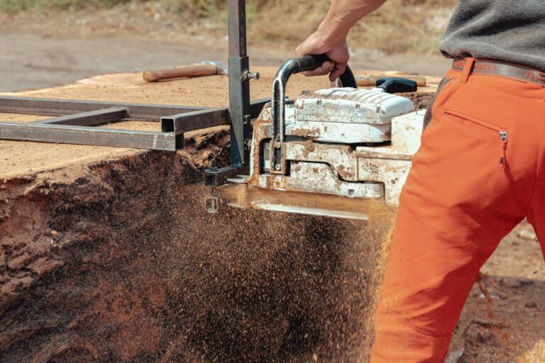 Close-up of a worker operating a chainsaw to cut wood at a construction site.